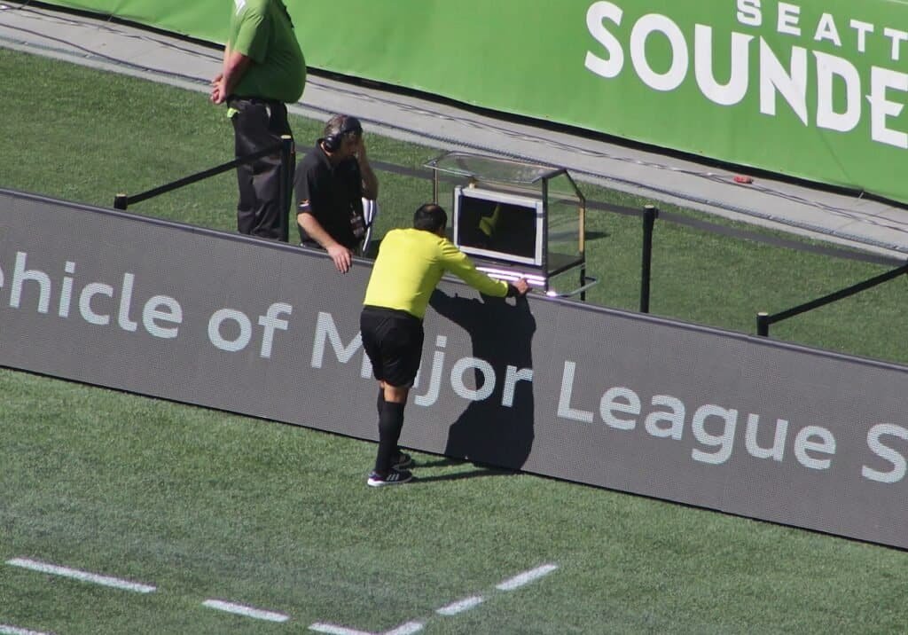 Árbitro de futebol consultando o monitor do VAR (Video Assistant Referee) à beira do campo durante uma partida